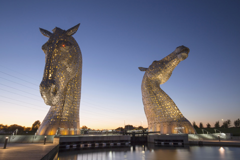 The flood-lit Kelpies horse-head statues at night time seen from the canal bank
