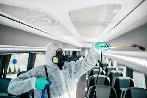 A cleaner wearing protective clothing sanitises the interior of a coach