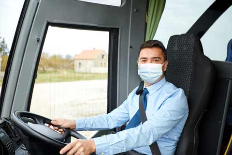 Friendly tour driver wearing a mask greets passengers on board