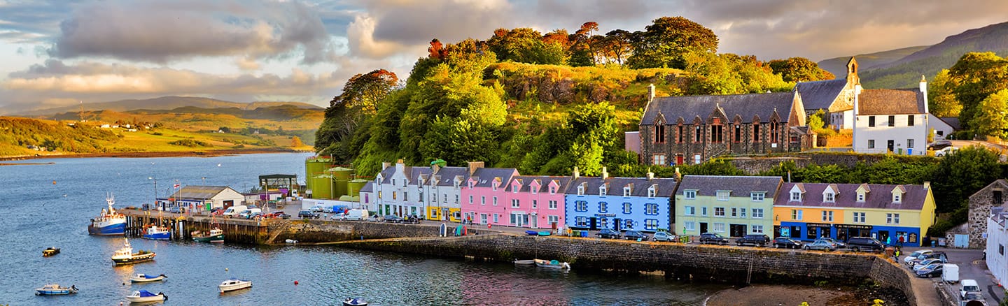 Pastel painted builings surround Portree harbour where fishing boats lie at anchor 