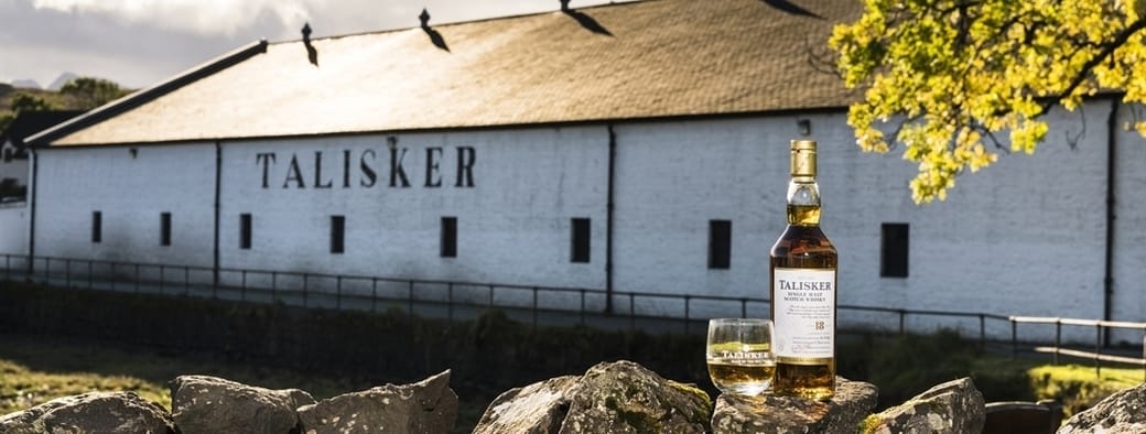 A glass and bottle of Talisker Malt Whisky placed on a wall outside the white-washed buildings of Talisker Distillery