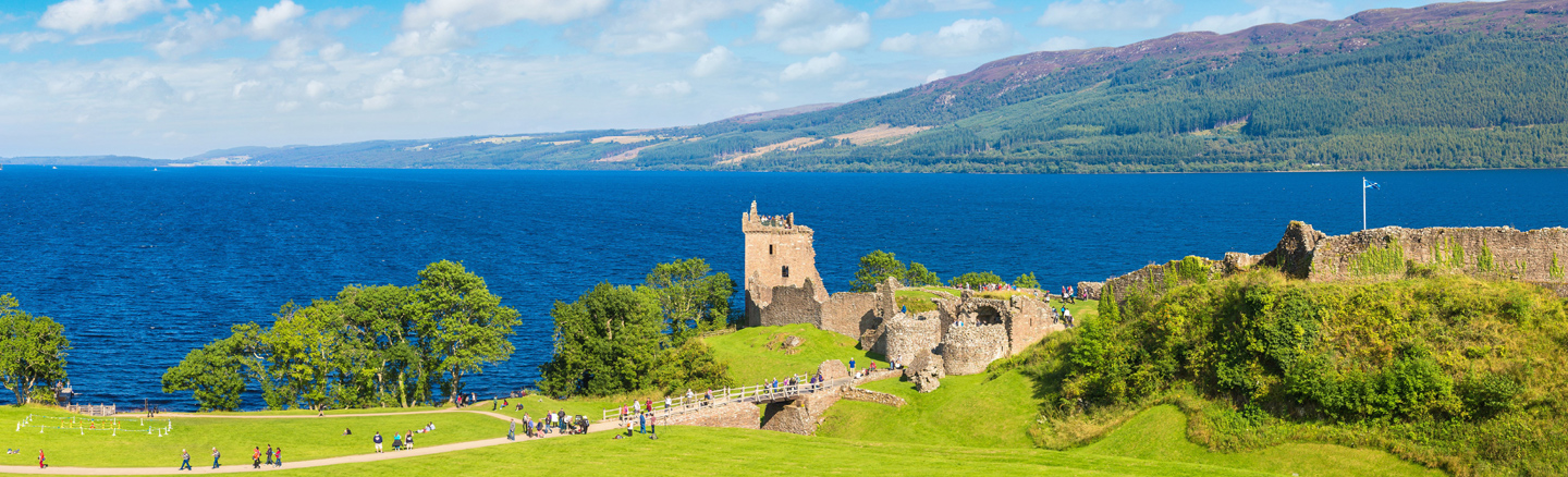 Summer view of Urquart Castle overlooking the bright blue waters of Loch Ness