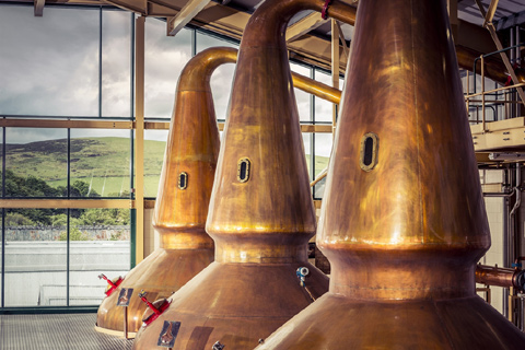 Three large copper stills housed in a glass-fronted building at Glenlivet Distillery