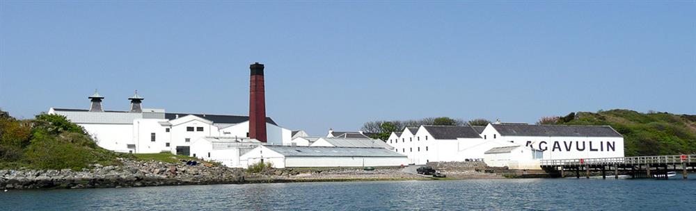A waterside view of Lagavulin Distillery showing the whitewashed buildings, red-painted chimney and famous twin-pagodas