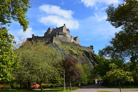 Edinburgh castle pictured sitting on rock amidst trees and flowers in Princes Street Gardens