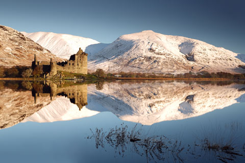 Castle and snow covered mountains reflected in still loch in Winter