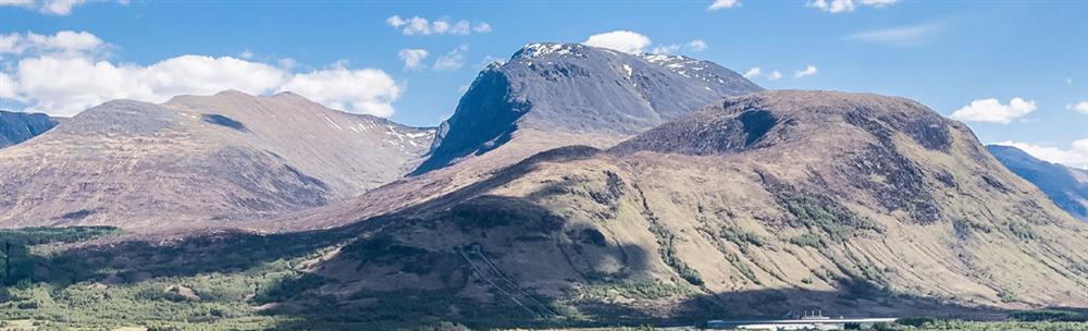 Panoramic view of Ben Nevis in bright sunshine and blue sky with scattered white clouds
