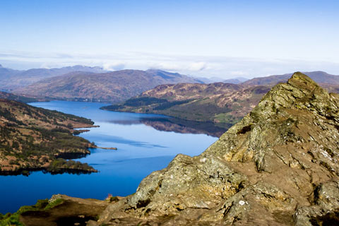 Loch Katrine with mountains on either side on bright day with clear blue sky