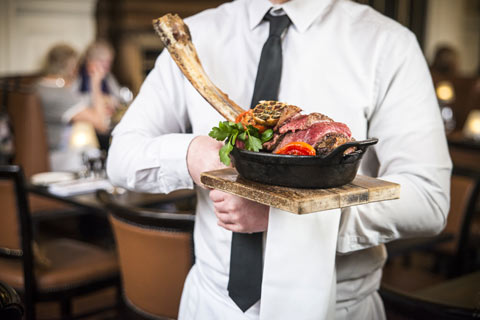 Waiter in white shirt and black tie carrying basket with steak